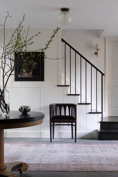 a room with a table, chair and vase on the floor next to a stair case