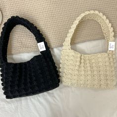 two purses sitting on top of a bed next to each other, one black and one white