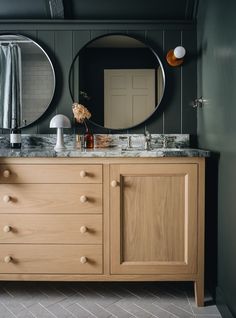 a bathroom vanity with two round mirrors above it and a wooden cabinet underneath the mirror