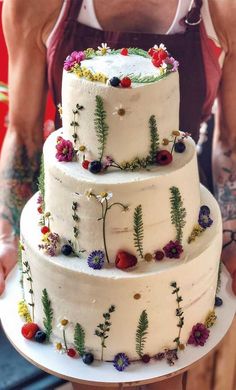 a man holding a three tiered cake with flowers and plants on the bottom layer