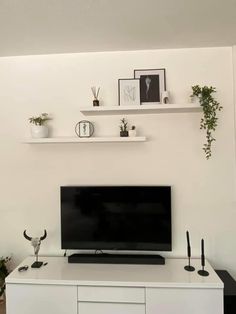 a flat screen tv sitting on top of a white entertainment center next to potted plants