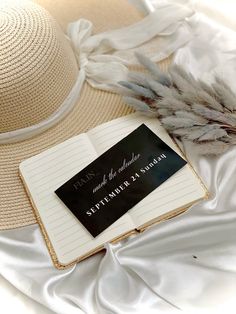 an open book sitting on top of a white bed next to a hat and feather