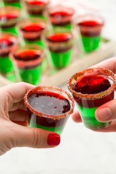 two hands holding small cups filled with red and green jellos next to each other