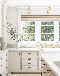 a kitchen with white cabinets and marble counter tops, gold pulls on the cabinet doors