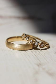 two gold wedding rings sitting on top of a wooden table