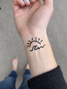 a woman's hand with a small tattoo on her wrist and the sun above it