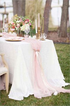 the table is set with pink and white flowers, candles, and plates on it