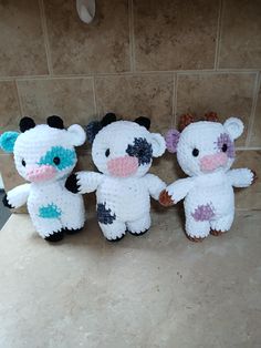 three small stuffed animals sitting next to each other on a tile counter top in a bathroom