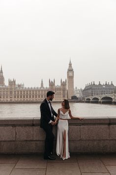 a man and woman standing next to each other in front of a body of water