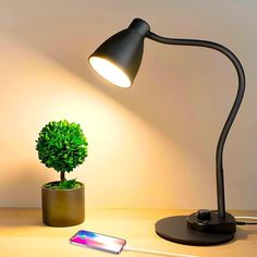 a desk lamp next to a cell phone and a potted plant on a table