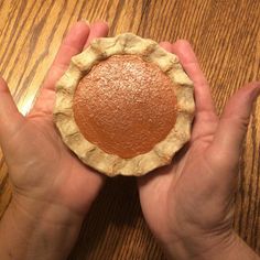 a hand holding a pie on top of a wooden table