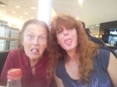 two women sitting at a table with food and drinks in front of them, posing for the camera