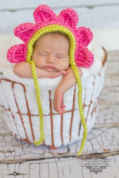 a newborn baby wearing a crocheted pink and green flower hat in a basket