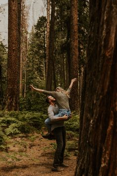 a man carrying a woman through the woods on his back while she holds him in the air