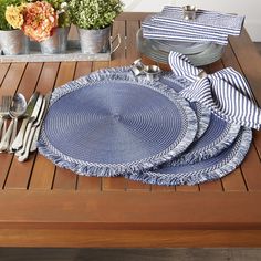 a place setting on a wooden table with blue and white napkins, silverware and flowers