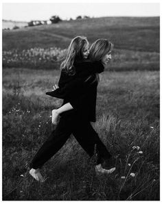 two women are walking through the grass in black and white, one is carrying another woman