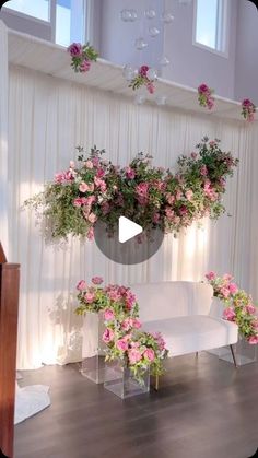 a white couch sitting in front of a window filled with pink flowers and greenery