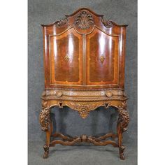 an antique wooden armoire with ornate carvings on the front and sides, sitting against a gray background