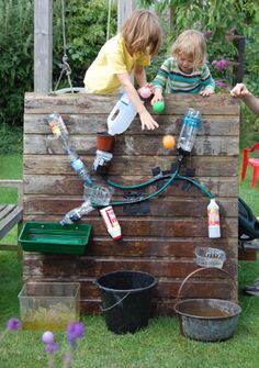 two children are playing outside on a small structure made out of bricks and plastic bottles