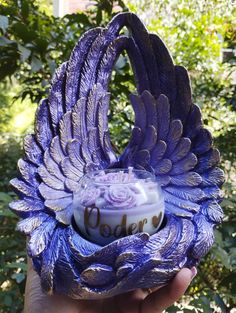 a hand holding a purple bird shaped container with flowers on it's body and wings