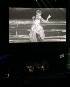 a woman is standing in front of a large screen on the stage at a concert