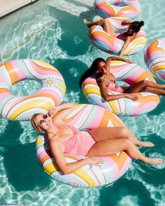 three women in swimsuits floating on rafts in a pool with sunbathers