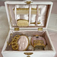 an open white box with gold trimmings and other items in it on a bed