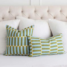 two green and blue pillows sitting on top of a white couch next to each other