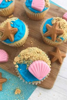 cupcakes with blue frosting and pink icing are on a wooden board