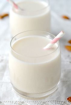 a glass filled with milk sitting on top of a table next to almonds and nuts