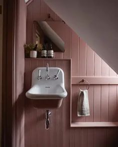 a white sink sitting under a window next to a wooden wall in a room with pink walls