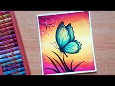 a blue butterfly sitting on top of a piece of paper next to crayons