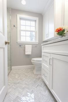 a bathroom with white cabinets and marble flooring is pictured in this image, there is a window above the toilet