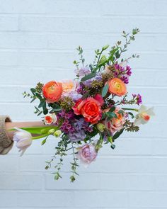 a person holding a bouquet of flowers in their hands with a brick wall behind them