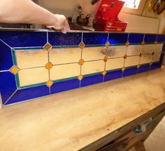 a blue and yellow tiled counter top with a hand reaching for the tile on it