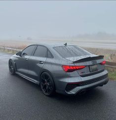 the rear end of a gray car driving on a foggy road