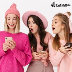 three young women wearing hats looking at their cell phones and making funny faces while standing next to each other