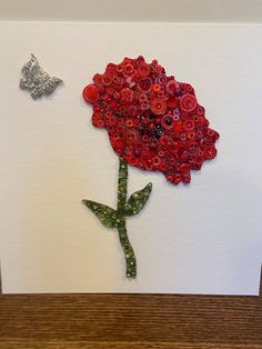 a red flower and butterfly on a white card with wood frame in the middle, sitting on a wooden table