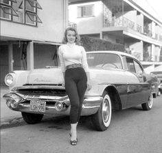 a black and white photo of a woman standing next to a car