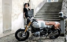 a woman standing next to a motorcycle parked on the side of a road near stairs