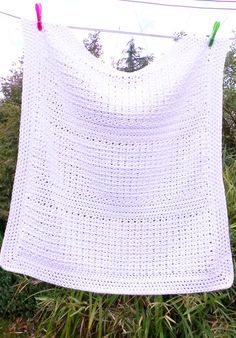 a white crocheted blanket hanging on a clothes line with two green pins in it