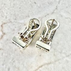 two pairs of silver colored metal clips on a white marble surface with small holes in the middle