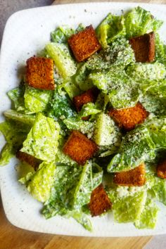 a white plate topped with lettuce and croutons covered in parmesan cheese