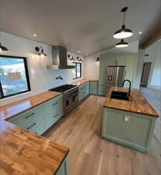 an empty kitchen with wooden counter tops and green cabinetry, along with stainless steel appliances