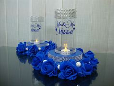 two wedding cake stands with blue roses and candles in them on a glass table top