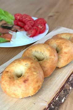 three bagels sitting on top of a cutting board next to a plate of vegetables