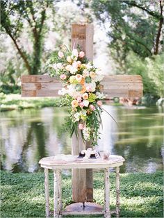 a cross with flowers on it sitting in the grass next to a lake and trees