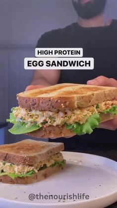 a man is holding up a sandwich with egg and lettuce in front of him