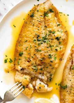 two pieces of fish on a plate with lemon sauce