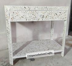 a white table with an intricate design on it's top and bottom shelf in the middle